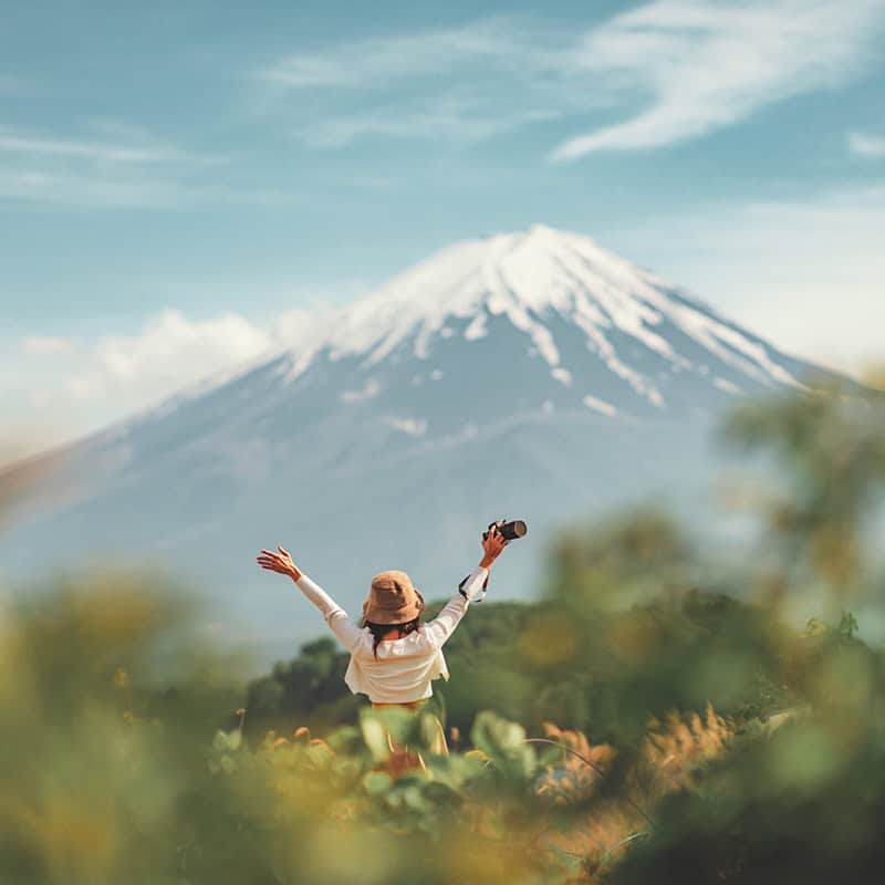 Woman with arms raised in front of snow-capped mountain.
