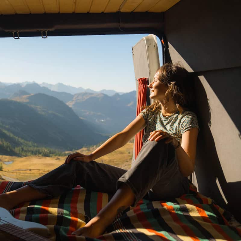 Serene woman sitting with guitar in camper van in mountains during road trip