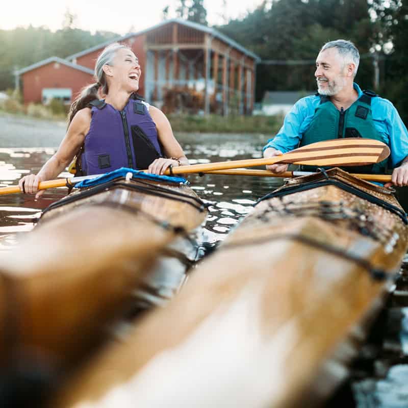 Seniors taking on the world! A mature couple in their late 50's enjoy paddling their kayaks on a relaxing vacation in Gig Harbor, Washington, the sun shining on the water of the Puget Sound. A depiction of health and relationship in later years.