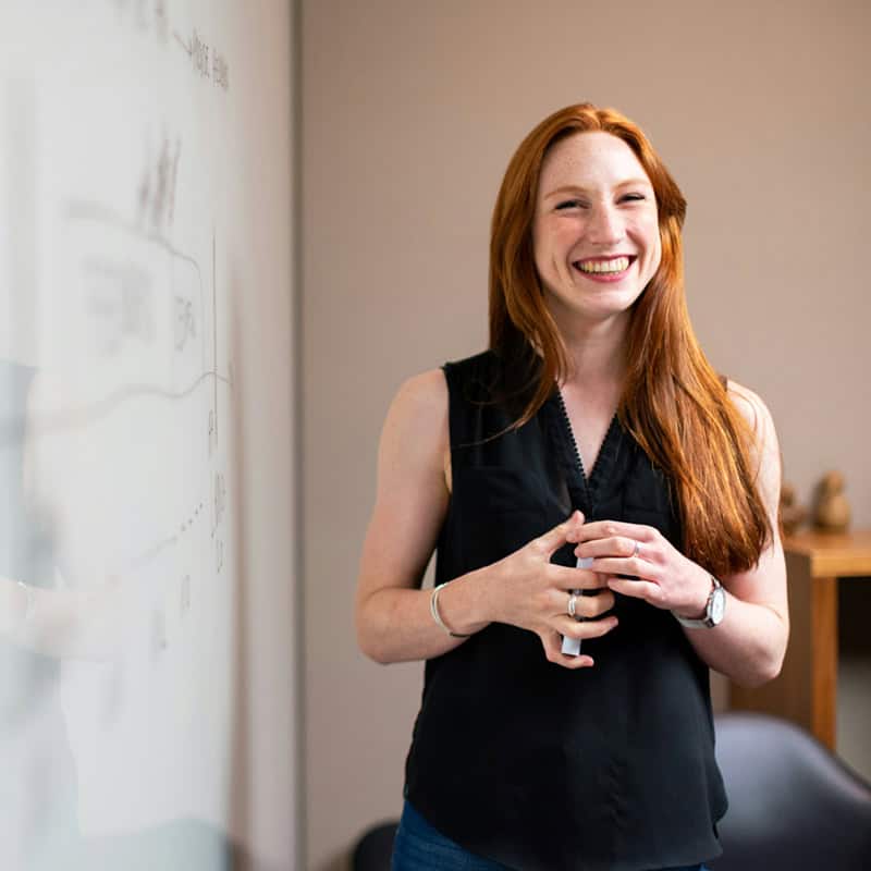 woman business owner smiles by a white board.